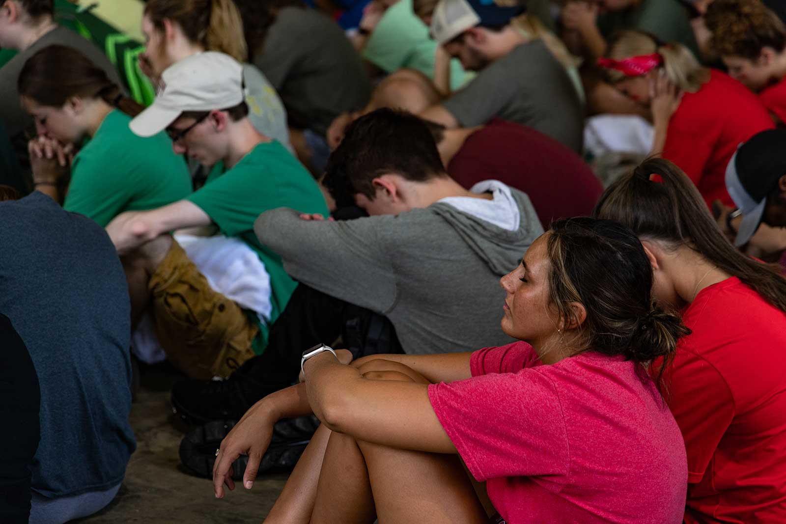 students praying in large group while sitting on the floor